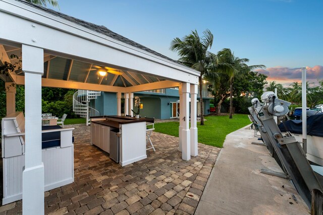 patio terrace at dusk with a gazebo, exterior bar, and a yard