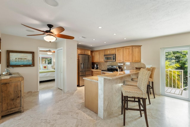 kitchen featuring appliances with stainless steel finishes, a breakfast bar, decorative backsplash, light stone counters, and kitchen peninsula