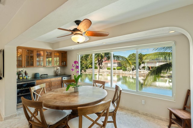 dining room featuring bar area, beverage cooler, ceiling fan, and a water view