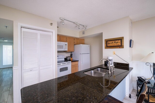 kitchen featuring sink, white appliances, rail lighting, a textured ceiling, and dark stone counters