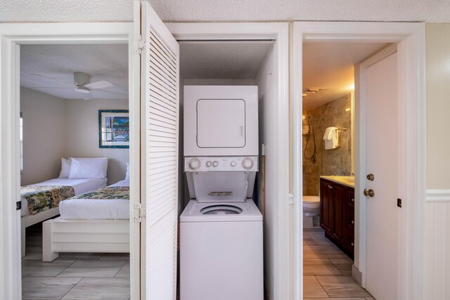 clothes washing area with ceiling fan, stacked washer and clothes dryer, and a textured ceiling