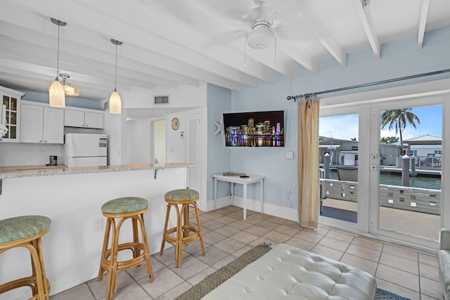 kitchen featuring light tile patterned floors, a kitchen breakfast bar, white fridge, beamed ceiling, and white cabinets