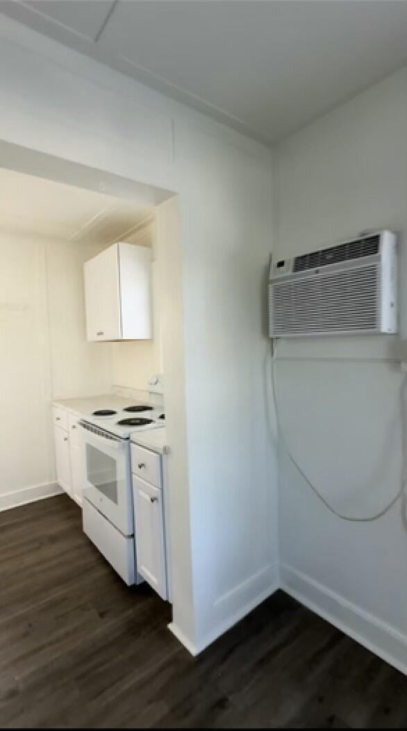 kitchen with dark hardwood / wood-style floors, a wall mounted AC, white cabinets, and white range with electric stovetop