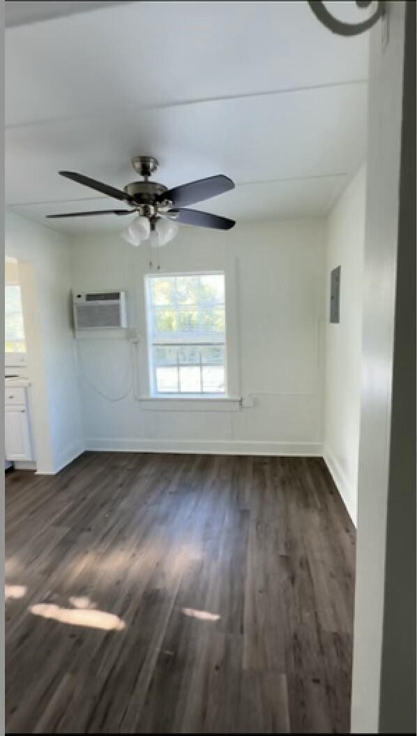 spare room with ceiling fan, dark hardwood / wood-style flooring, electric panel, and a wall unit AC