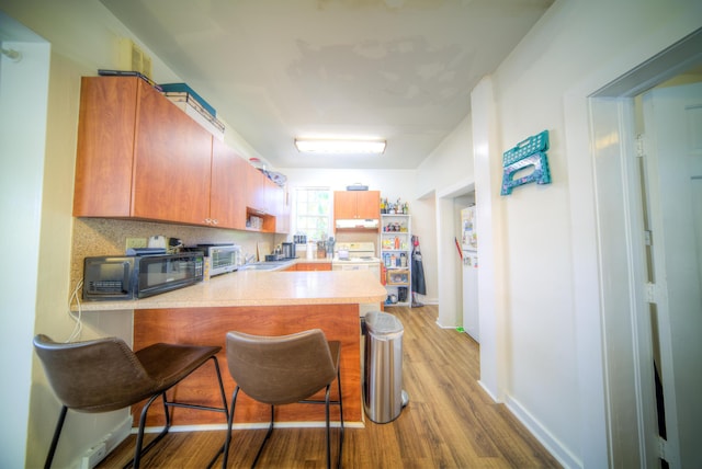 kitchen featuring tasteful backsplash, light wood-type flooring, a kitchen breakfast bar, and kitchen peninsula