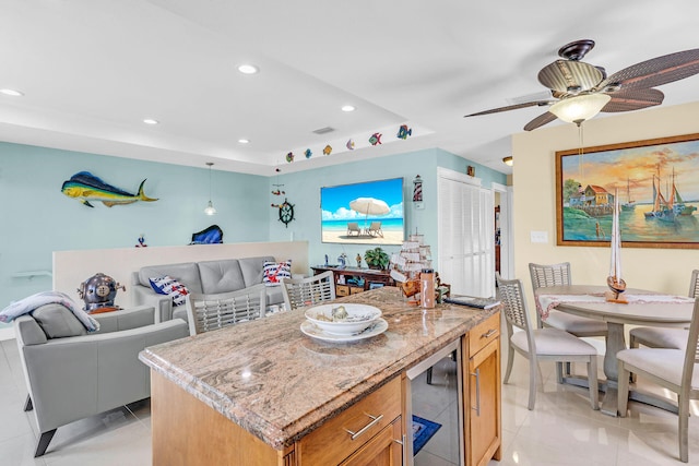 kitchen featuring light tile patterned flooring, a kitchen island, ceiling fan, beverage cooler, and light stone countertops