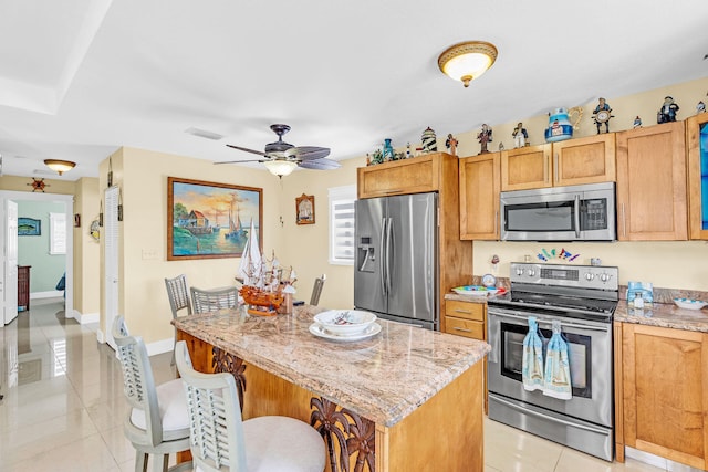 kitchen with a breakfast bar, light tile patterned floors, a kitchen island, stainless steel appliances, and light stone countertops