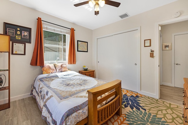 bedroom with visible vents, a ceiling fan, wood finished floors, a closet, and baseboards