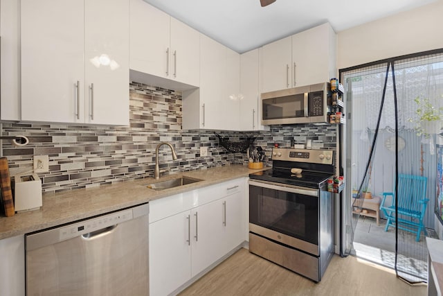 kitchen with a sink, tasteful backsplash, white cabinetry, stainless steel appliances, and light wood finished floors