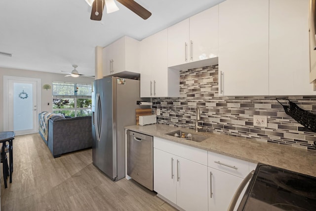 kitchen featuring light wood finished floors, a sink, white cabinets, appliances with stainless steel finishes, and tasteful backsplash