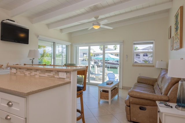 kitchen with light tile patterned floors, ceiling fan, vaulted ceiling with beams, white cabinets, and a kitchen bar