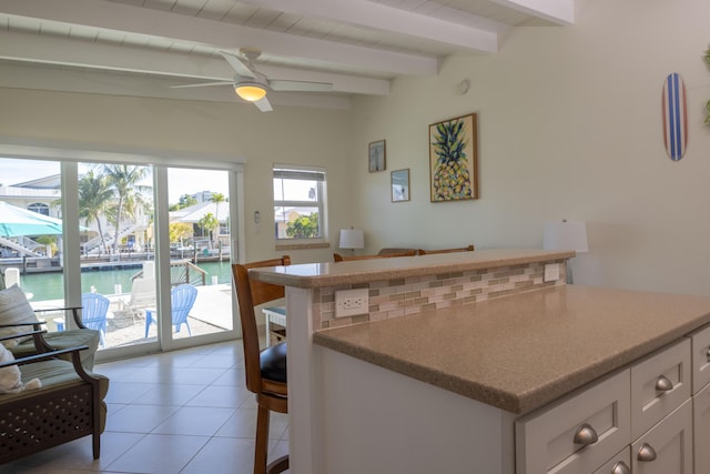 kitchen with light tile patterned floors, a breakfast bar area, ceiling fan, beam ceiling, and a water view