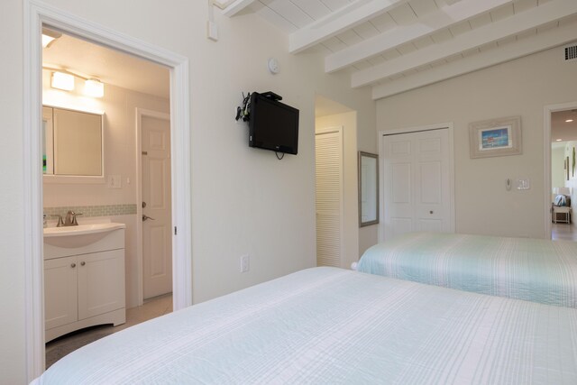 bedroom with connected bathroom, sink, and vaulted ceiling with beams