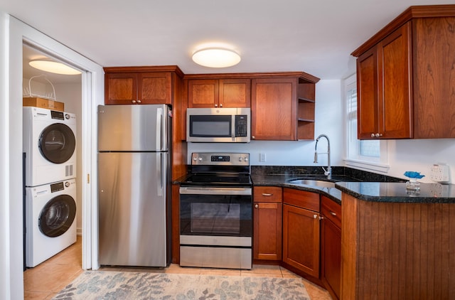 kitchen featuring stacked washing maching and dryer, appliances with stainless steel finishes, sink, dark stone counters, and light tile patterned floors