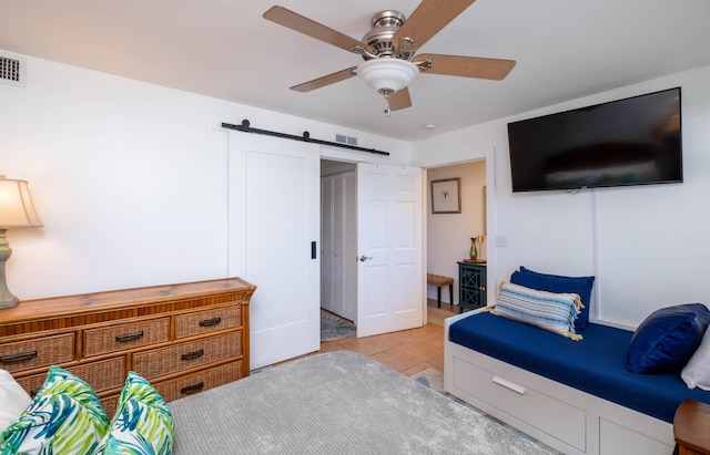 bedroom with a barn door, light tile patterned floors, and ceiling fan