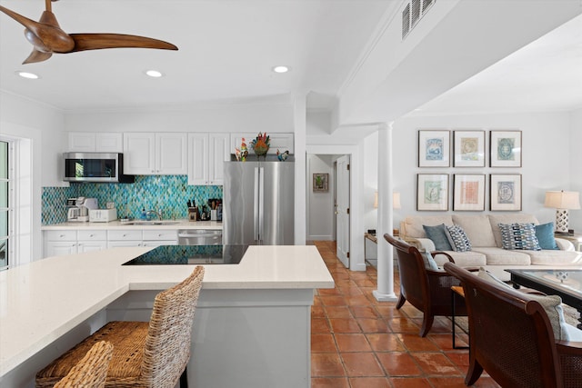 kitchen featuring crown molding, white cabinetry, stainless steel appliances, decorative columns, and decorative backsplash