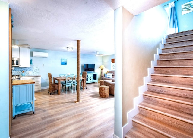 staircase with wood-type flooring, a wall unit AC, ceiling fan, and a textured ceiling