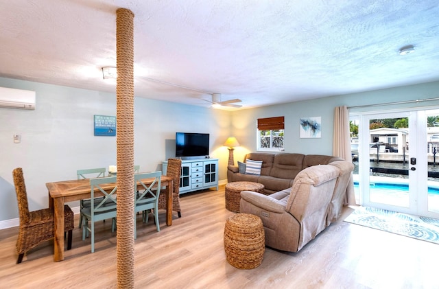 living room featuring ceiling fan, light hardwood / wood-style flooring, a wall unit AC, and a textured ceiling