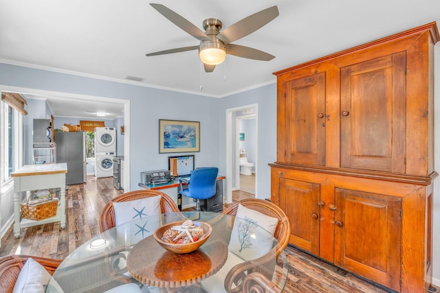 dining area featuring stacked washer / drying machine, wood-type flooring, ornamental molding, and ceiling fan