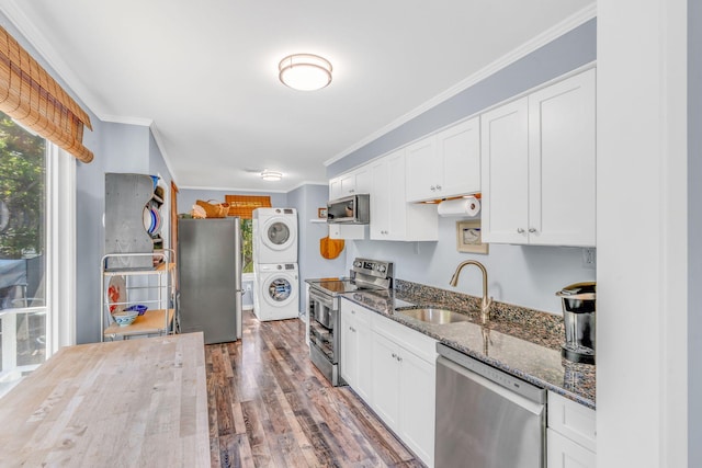 kitchen featuring white cabinetry, stacked washer / dryer, dark stone countertops, and appliances with stainless steel finishes