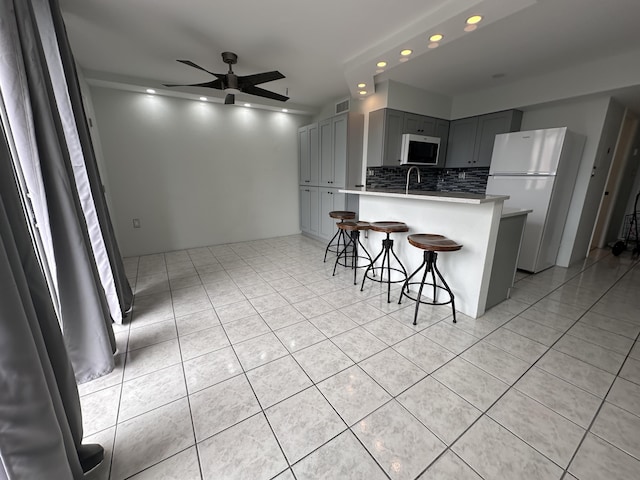 kitchen with gray cabinets, white refrigerator, a kitchen bar, decorative backsplash, and kitchen peninsula