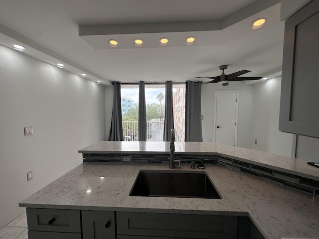 kitchen with light stone countertops, sink, kitchen peninsula, and gray cabinetry