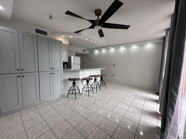 kitchen with light tile patterned floors, ceiling fan, refrigerator, gray cabinetry, and a kitchen breakfast bar