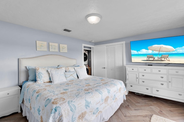 bedroom with parquet floors, stacked washer / dryer, and a closet