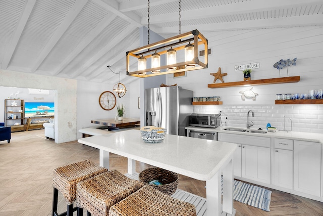 kitchen featuring sink, white cabinetry, stainless steel appliances, a kitchen breakfast bar, and decorative light fixtures