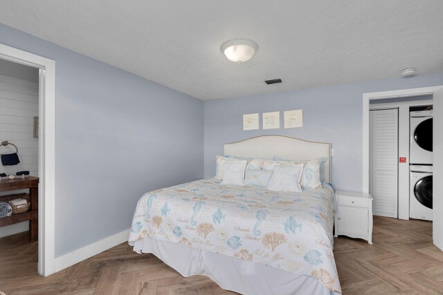 bedroom featuring light parquet floors and stacked washing maching and dryer