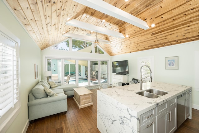 kitchen with dark hardwood / wood-style floors, vaulted ceiling with skylight, an island with sink, sink, and light stone countertops