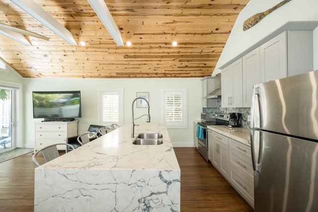 kitchen featuring sink, vaulted ceiling with beams, a center island with sink, appliances with stainless steel finishes, and light stone countertops