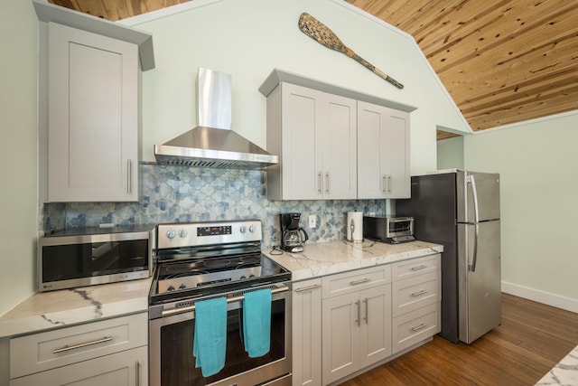 kitchen featuring appliances with stainless steel finishes, lofted ceiling, decorative backsplash, light stone counters, and wall chimney range hood