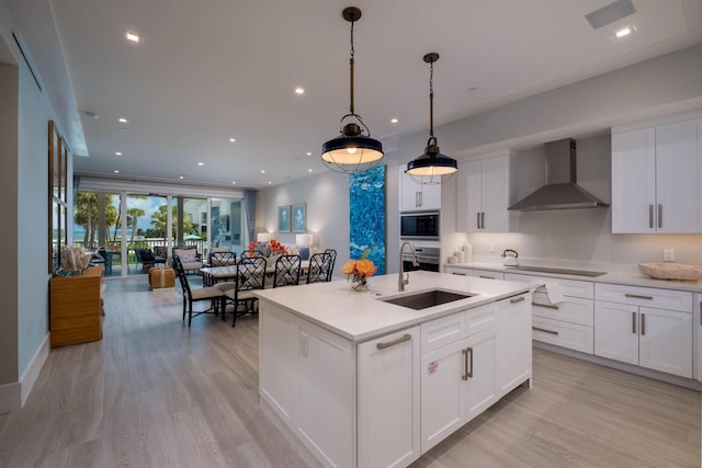 kitchen with wall chimney exhaust hood, sink, a center island with sink, pendant lighting, and black appliances