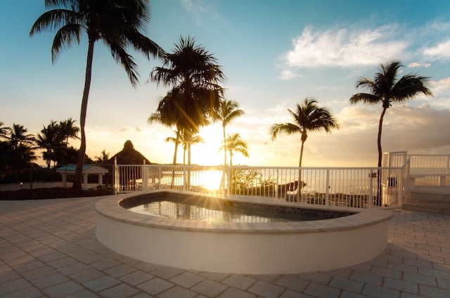 pool at dusk featuring a patio area and a hot tub