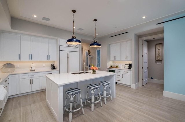 kitchen featuring white cabinetry, paneled built in refrigerator, sink, and a center island with sink