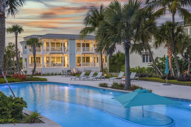 pool at dusk featuring ceiling fan and a patio