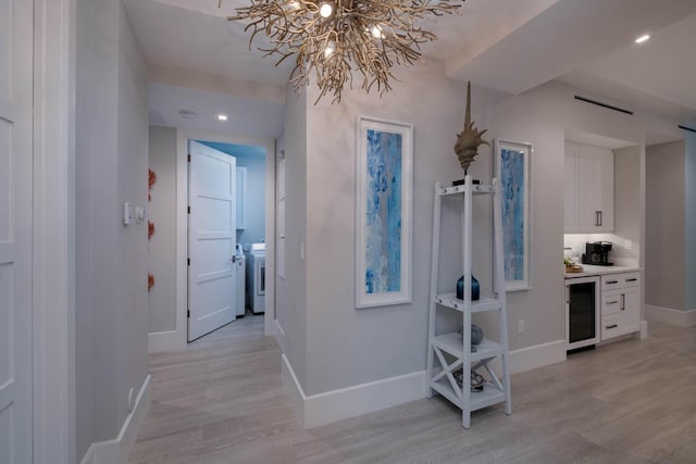 hallway with wine cooler, washer and clothes dryer, and light wood-type flooring