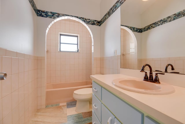 full bathroom with tile walls, vanity, tiled shower / bath combo, and toilet