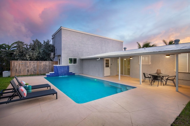 pool at dusk featuring pool water feature and a patio