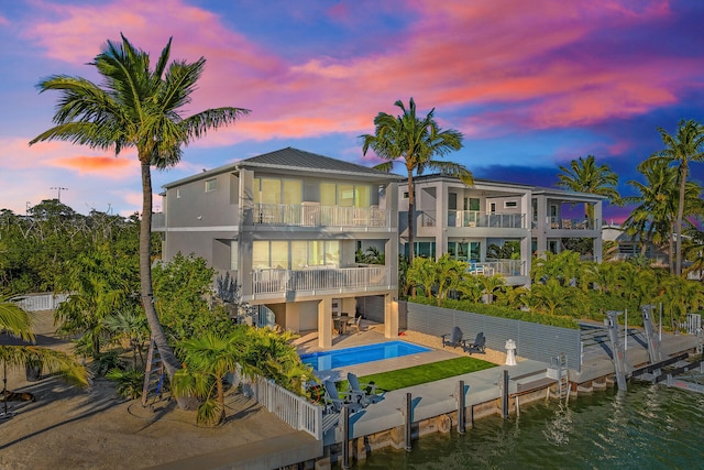 back house at dusk featuring a fenced in pool, a patio, a balcony, and a water view