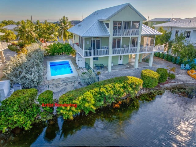 back house at dusk featuring a patio area, a sunroom, a balcony, and a water view