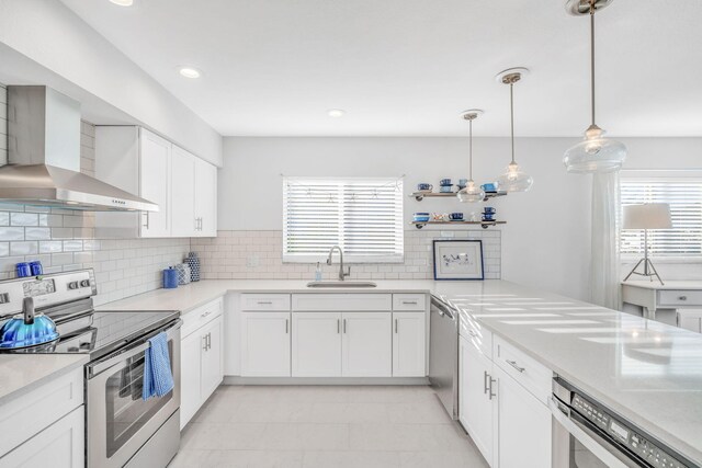 kitchen featuring appliances with stainless steel finishes, pendant lighting, sink, white cabinets, and wall chimney range hood