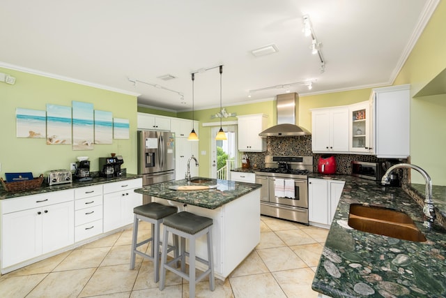 kitchen with appliances with stainless steel finishes, an island with sink, sink, a kitchen bar, and wall chimney range hood