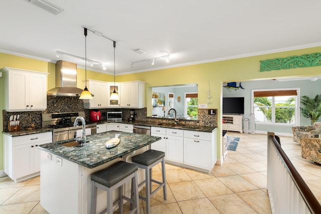 kitchen with decorative light fixtures, ventilation hood, sink, double oven range, and a kitchen island with sink