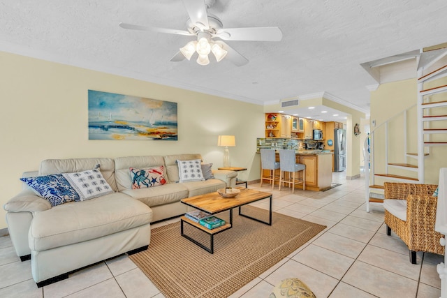 living room featuring ornamental molding, light tile patterned floors, ceiling fan, and a textured ceiling