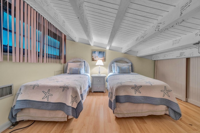 bedroom featuring hardwood / wood-style floors, track lighting, and beam ceiling