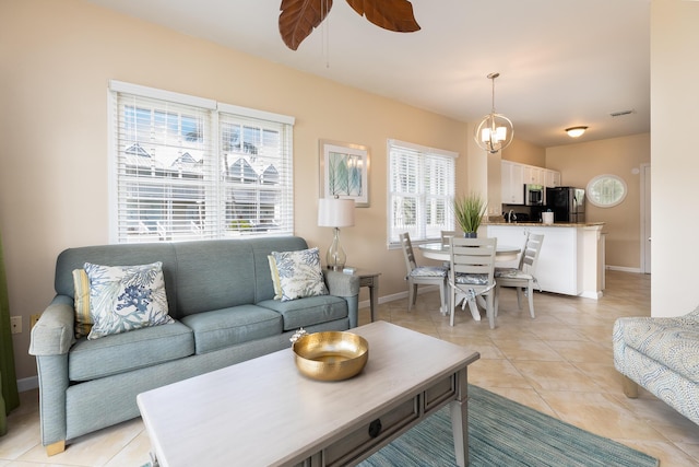 living area featuring ceiling fan with notable chandelier, visible vents, baseboards, and light tile patterned floors
