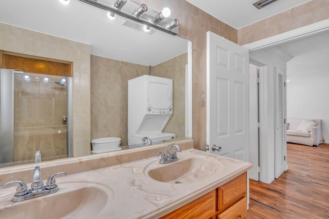 bathroom featuring stacked washing maching and dryer, tile walls, vanity, and toilet