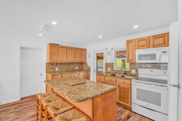 kitchen featuring sink, white appliances, a breakfast bar area, a center island, and light hardwood / wood-style floors